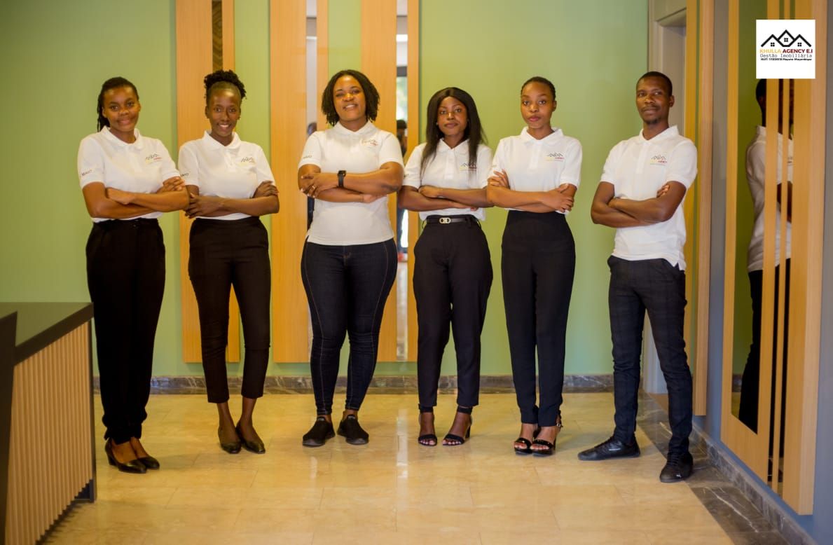 Six people in white shirts and black pants standing with arms crossed in a modern building.