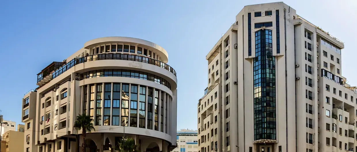 Two modern buildings against a clear blue sky. One is round, the other is rectangular.
