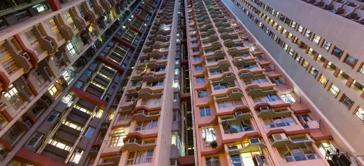 Low-angle view of high-rise apartment buildings at dusk, with illuminated windows and various shades of orange and beige.