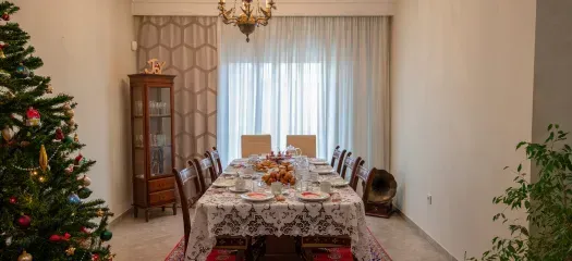 A decorated dining room with a long table set for a holiday meal. A Christmas tree stands to the left.
