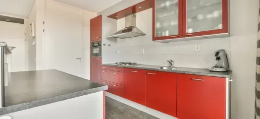 A modern kitchen with red cabinets, stainless steel appliances, and a white countertop.