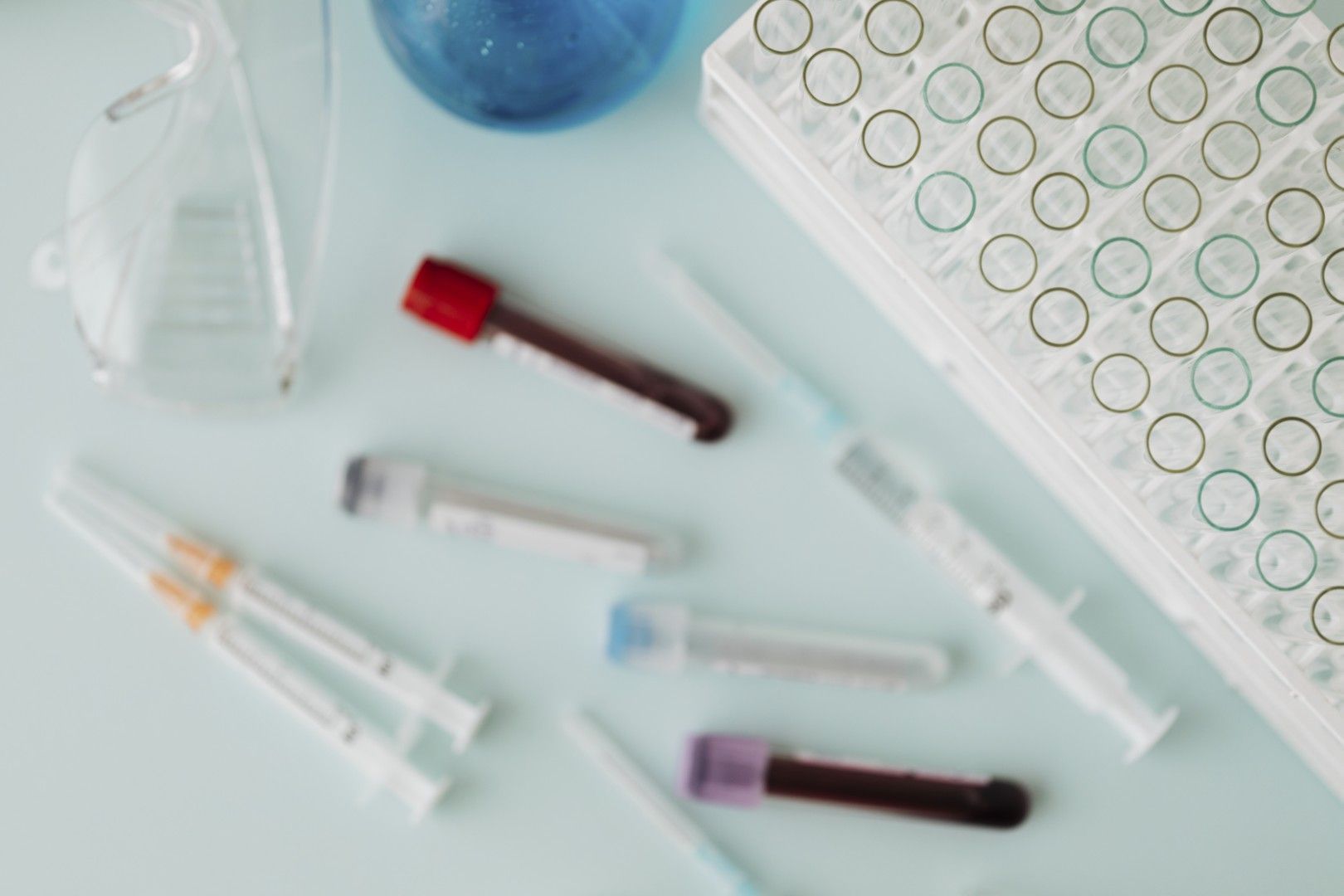 Material para análisis de sangre con viales, jeringas y una gradilla para tubos de laboratorio sobre una superficie clara
