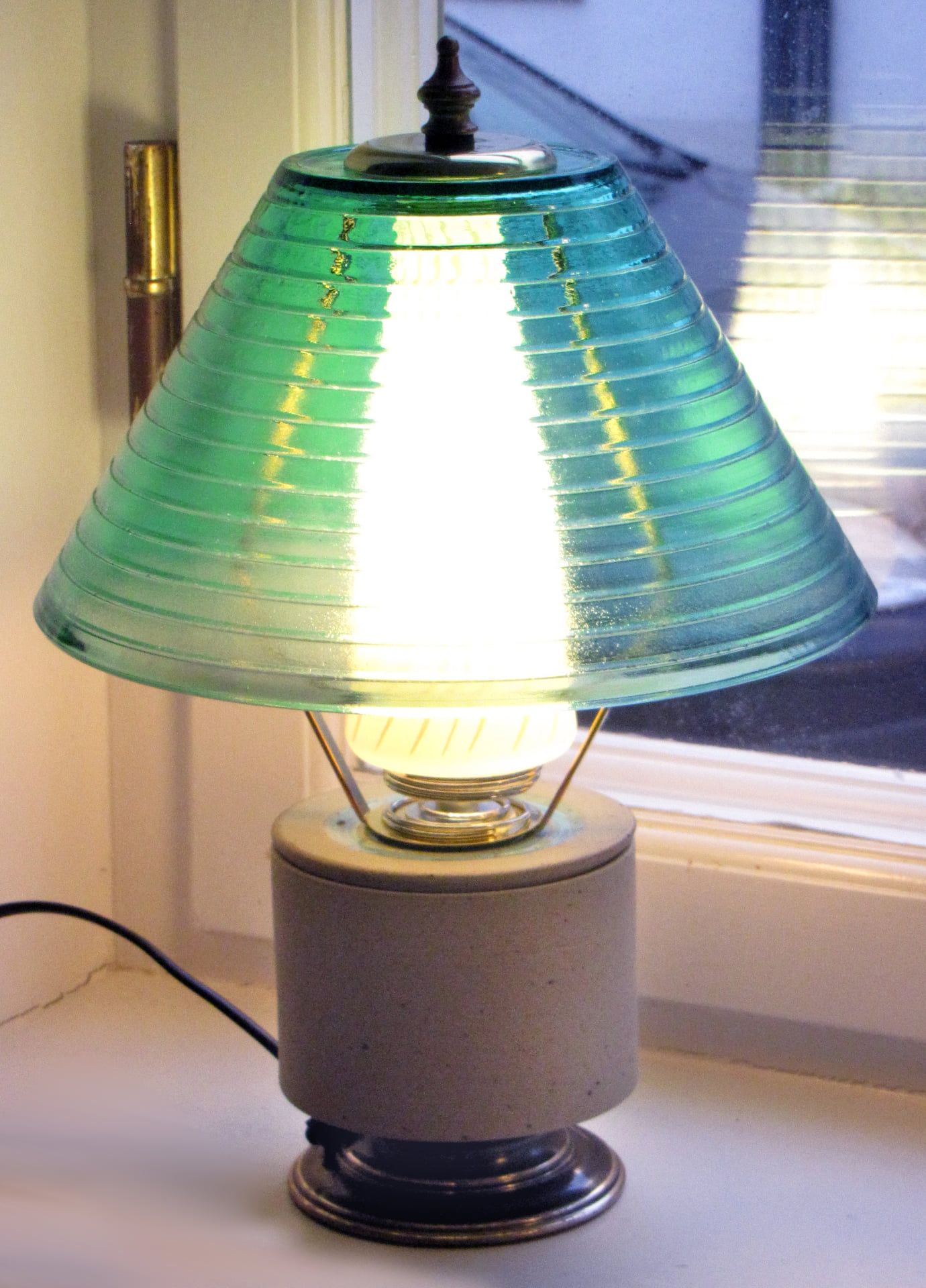 Grüne Glastischlampe leuchtet in der Dämmerung auf einer Fensterbank