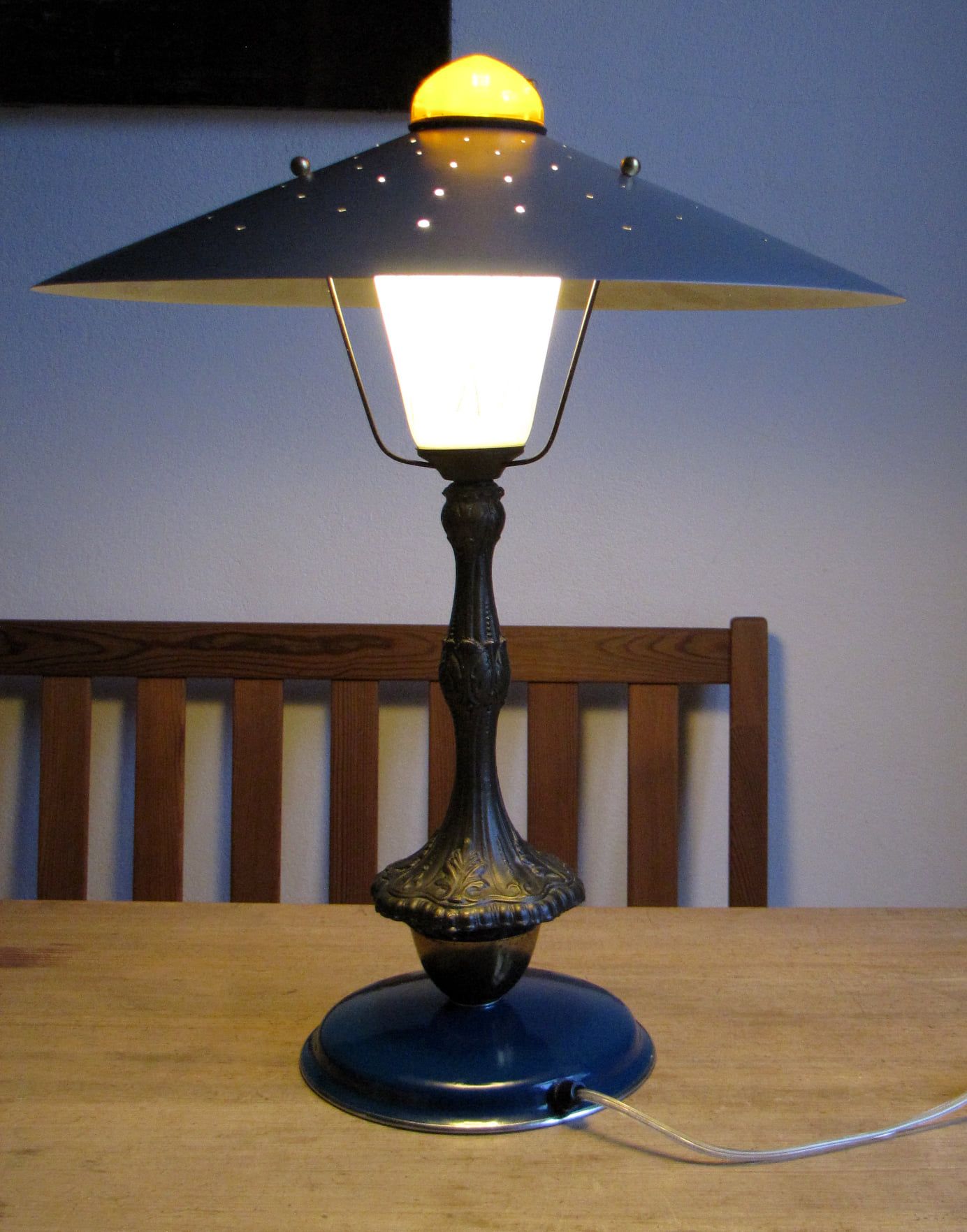 Tischlampe mit schwarzem Schirm, weißem Licht und blauem Fuß auf einem Holztisch