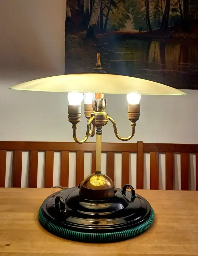 Vintage-Tischlampe aus Messing mit weißem Schirm auf einem Holztisch vor einem Wandgemälde.