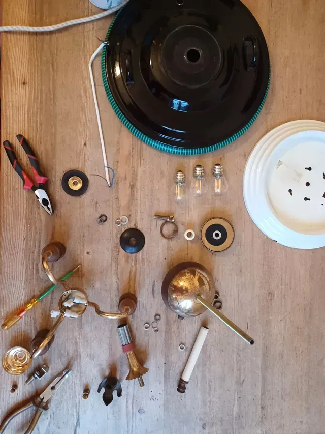 Verschiedene elektrische Bauteile und Werkzeuge lagen auf einem Holztisch, mittig um ein schwarzes, kreisförmiges Gerät angeordnet.