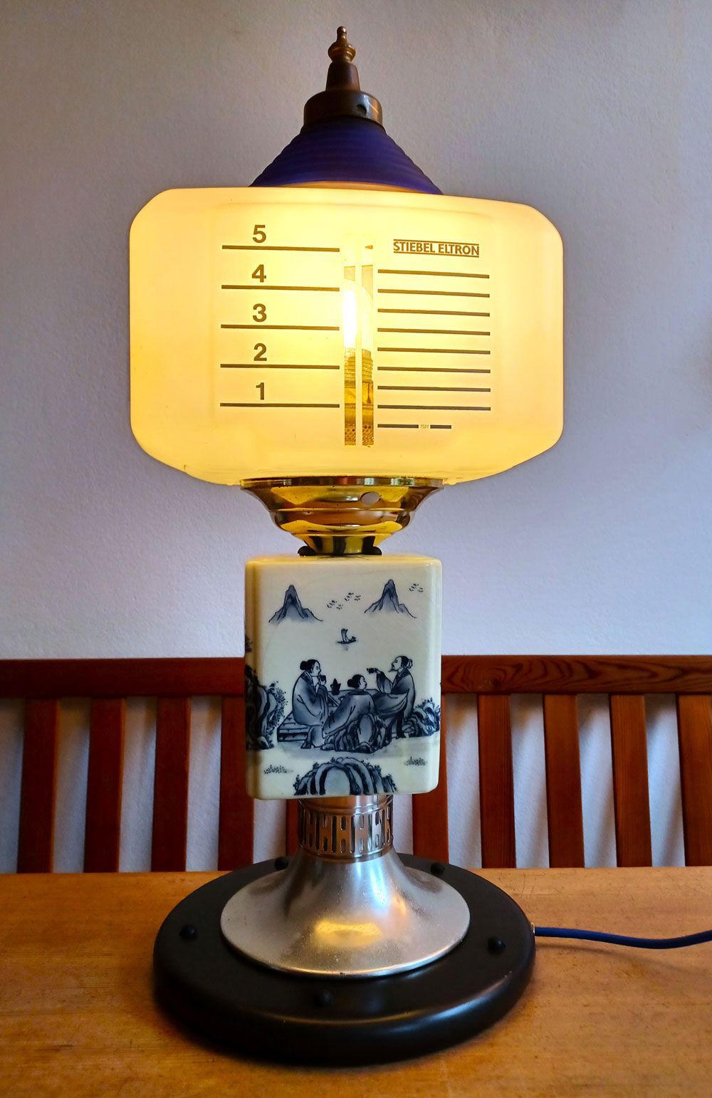 Eine einzigartige, wiederverwendete Lampe mit einem Schirm in Form einer Milchflasche und einem Keramiksockel im Delfter Stil auf einem Holztisch.