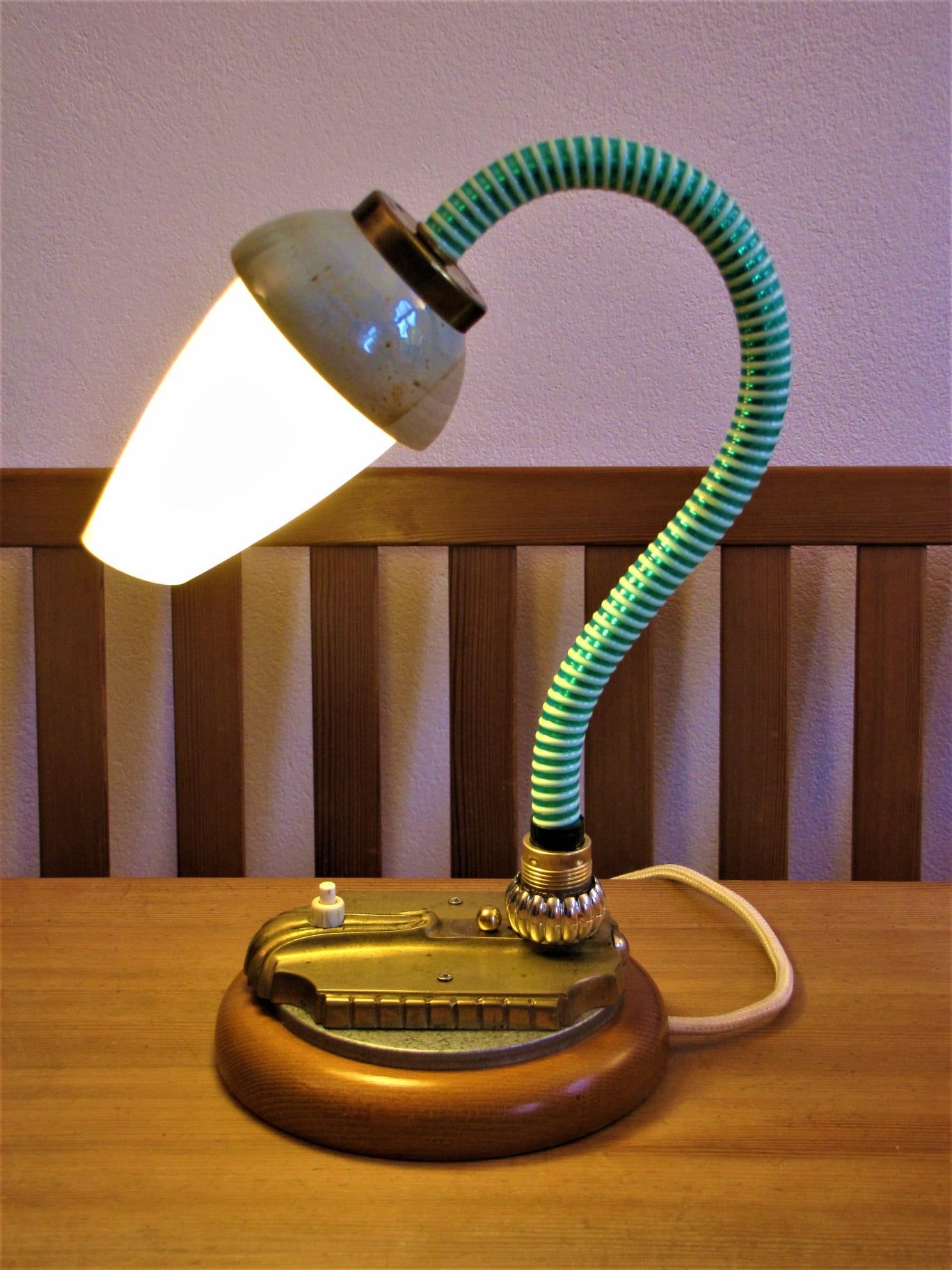 Kleine Vintage-Schreibtischlampe mit weißem Schirm und grünem, flexiblem Hals auf einem Holzsockel.