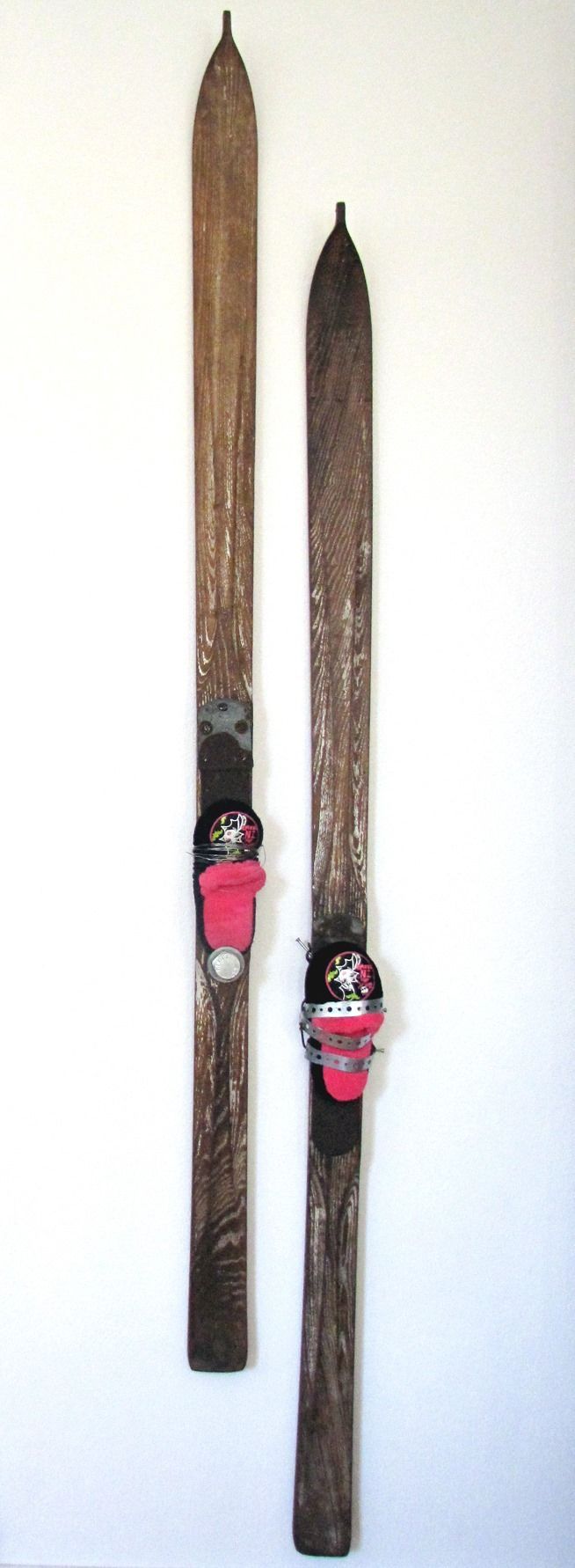 Zwei geschnitzte, skiähnliche Holzobjekte mit rot und schwarz bemalten Figuren vor weißem Hintergrund