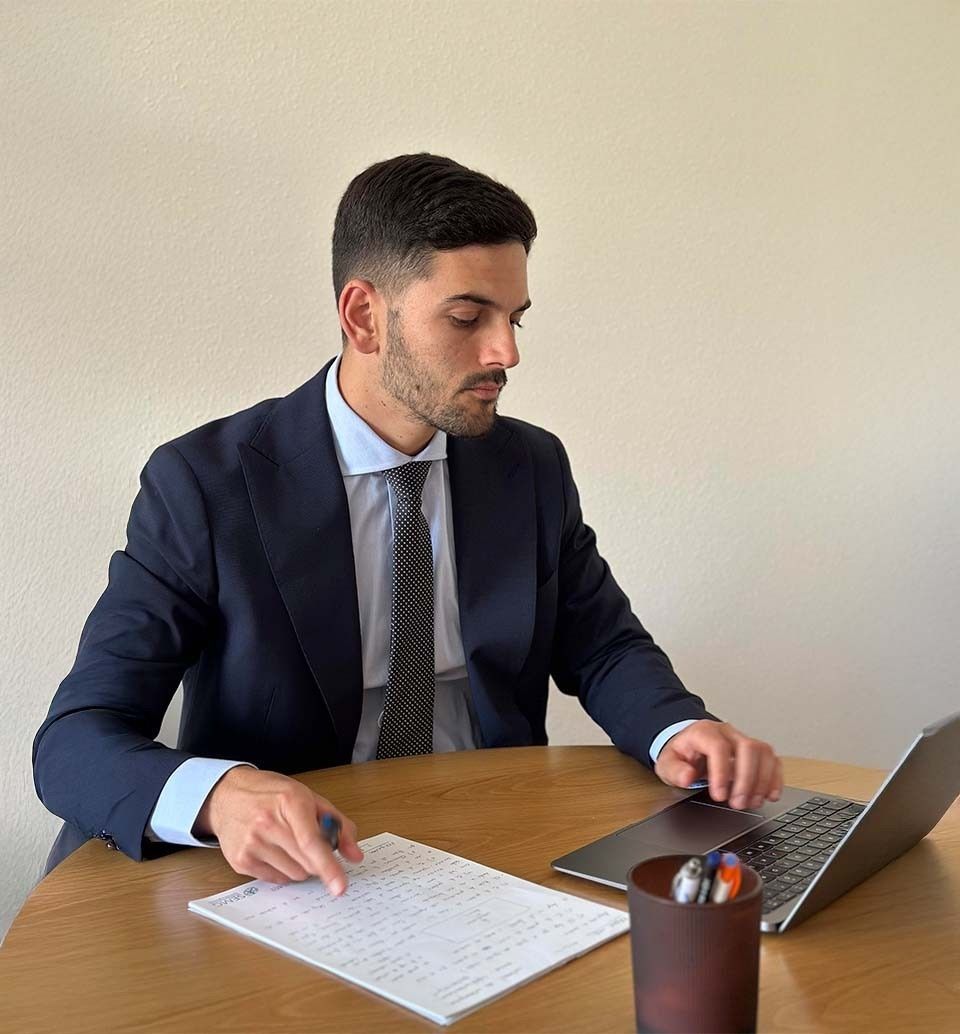 Hombre de traje trabajando en una computadora portátil y escribiendo en papel en una mesa de madera.