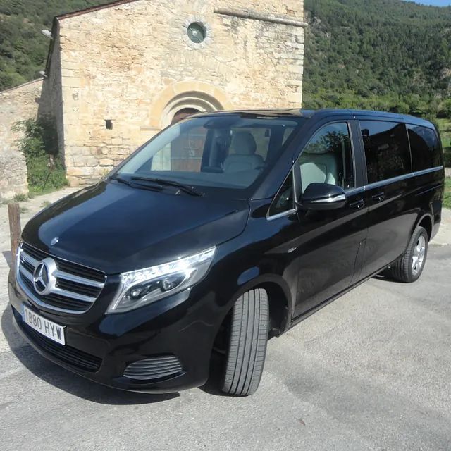 Una furgoneta Mercedes negra está estacionada frente a un edificio de piedra.