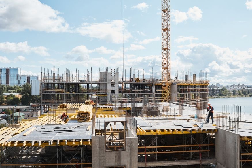 Construction site with a tower crane and workers on a partially built concrete structure under a blue sky