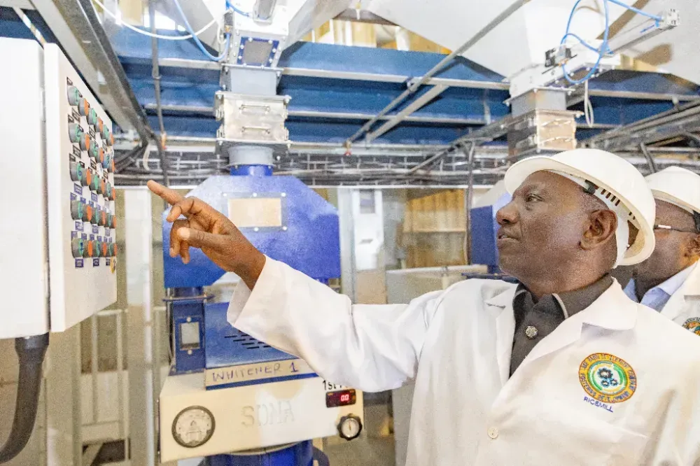 A man in a lab coat and hard hat is pointing at a machine.