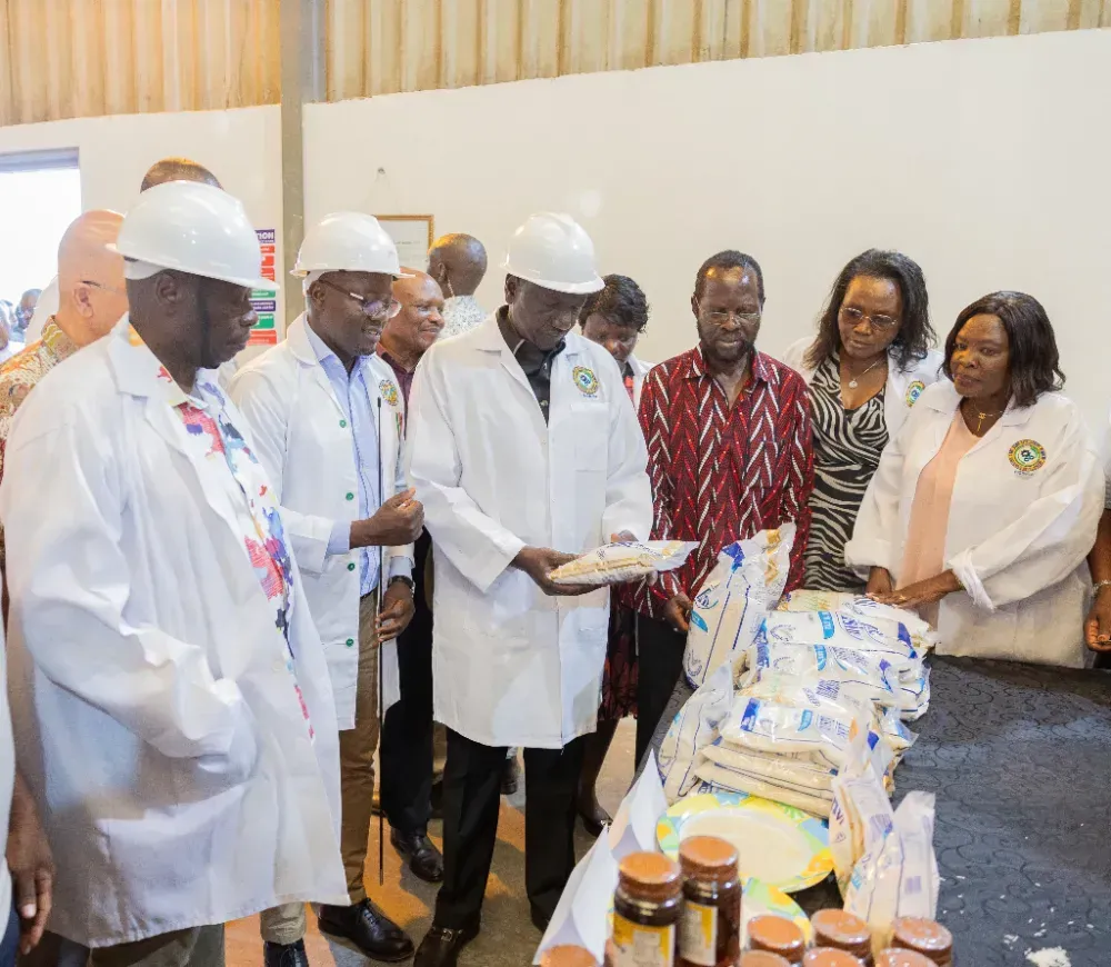 A group of people in white coats and hard hats are standing around a table.