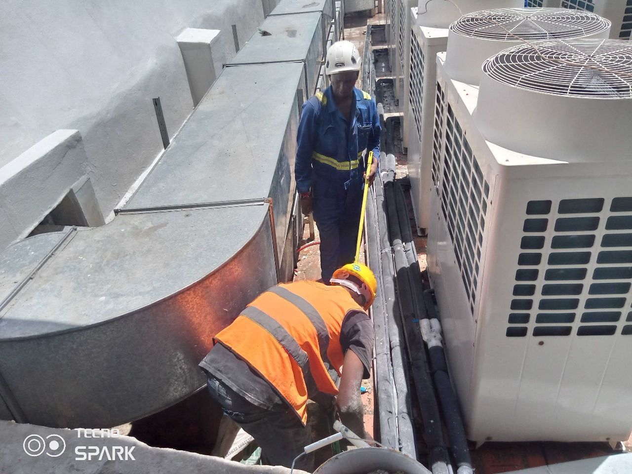 A man in an orange vest is working on an air conditioner