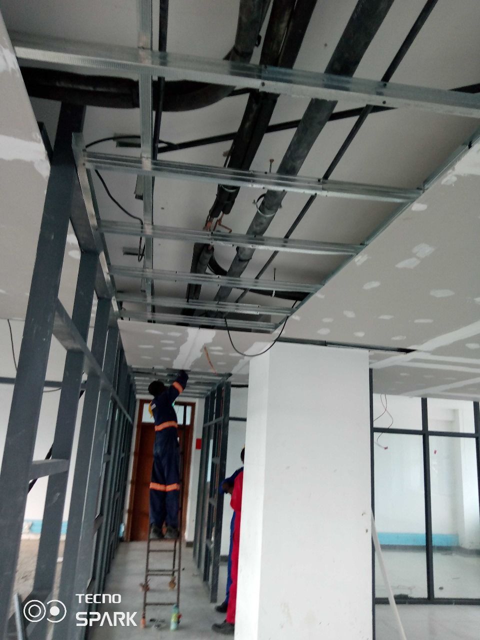 Two men are working on the ceiling of a building.