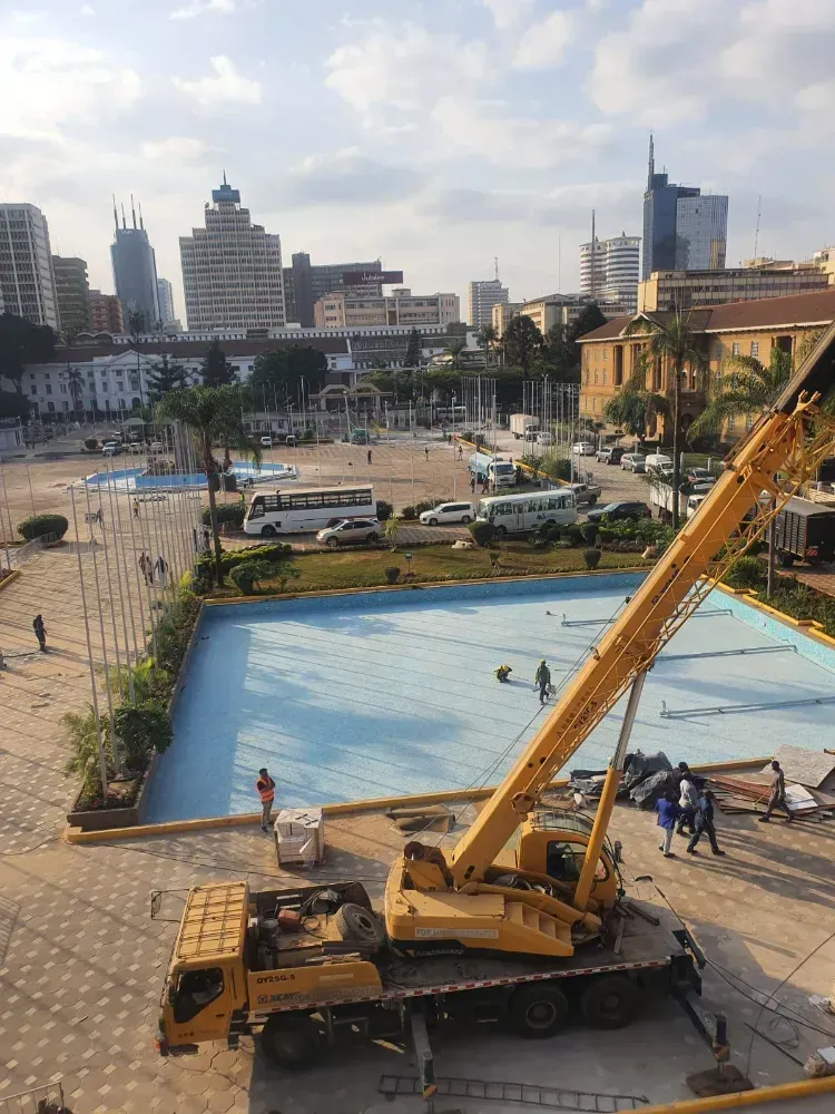 A large yellow crane is sitting in front of a swimming pool in a city.