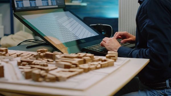 A man sitting at a table with a computer and a building model.