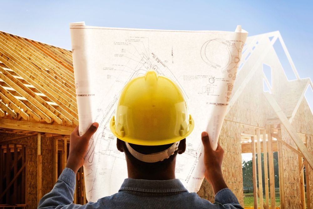 Construction worker in yellow hard hat reviewing blueprints at a house construction site