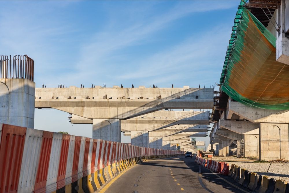 Construction site with concrete bridge spans, road barriers, and scaffolding under a blue sky