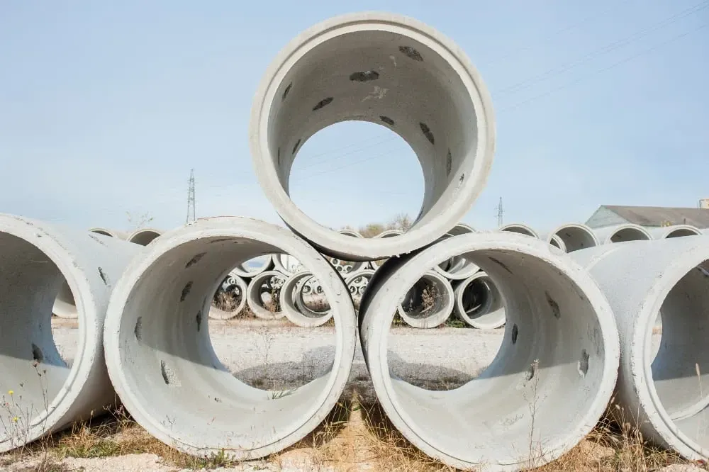 Stacked white concrete pipes in an outdoor construction yard under a blue sky