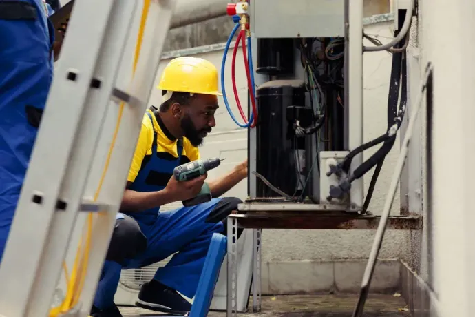 A man wearing a hard hat is working on an air conditioner.