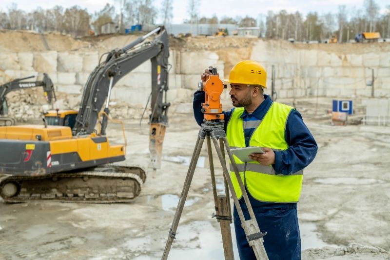 A construction worker is using aodolite on a tripod at a construction site.