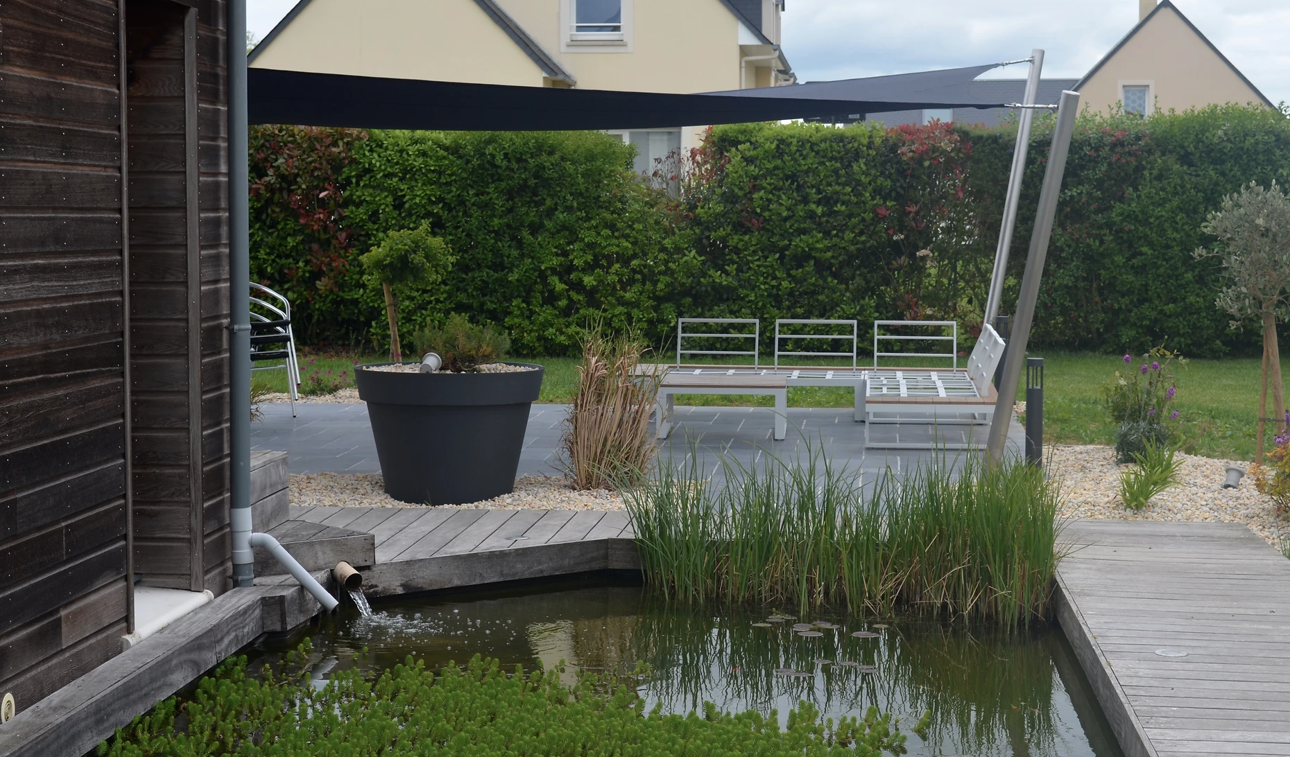 Voile d'ombrage près d'une mare, au-dessus d'une terrasse avec salon de jardin