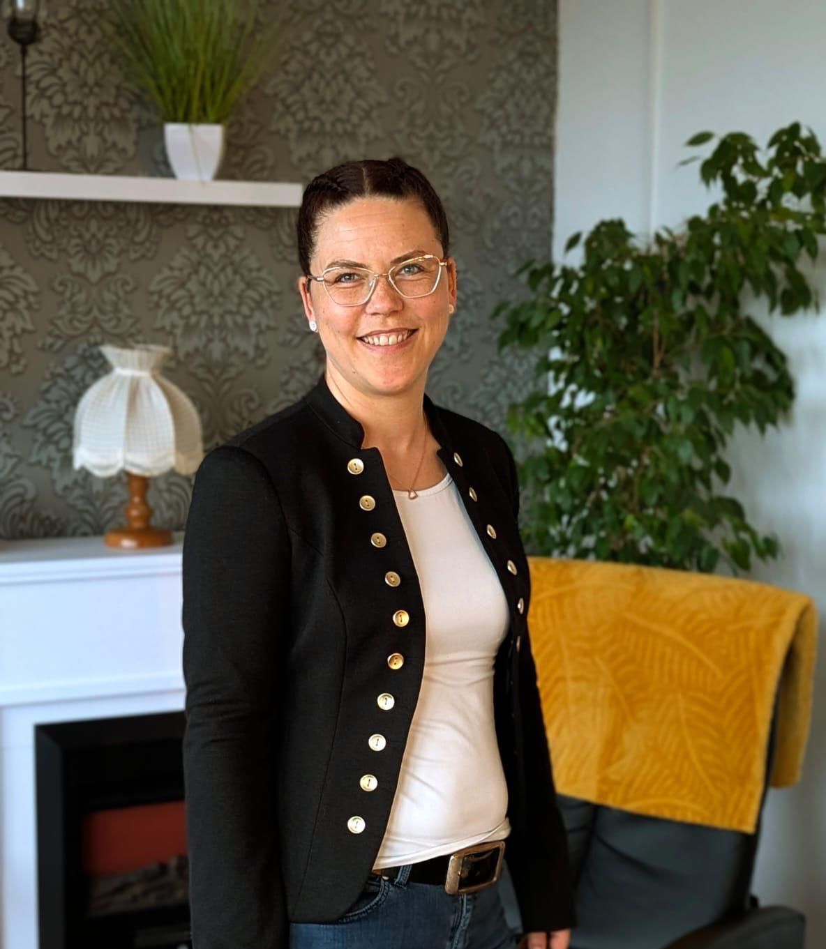 Eine Frau mit Brille und blauer Jacke steht vor einem Radio.