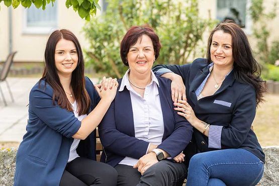 Drei Frauen posieren für ein Foto, während sie auf einer Bank sitzen.