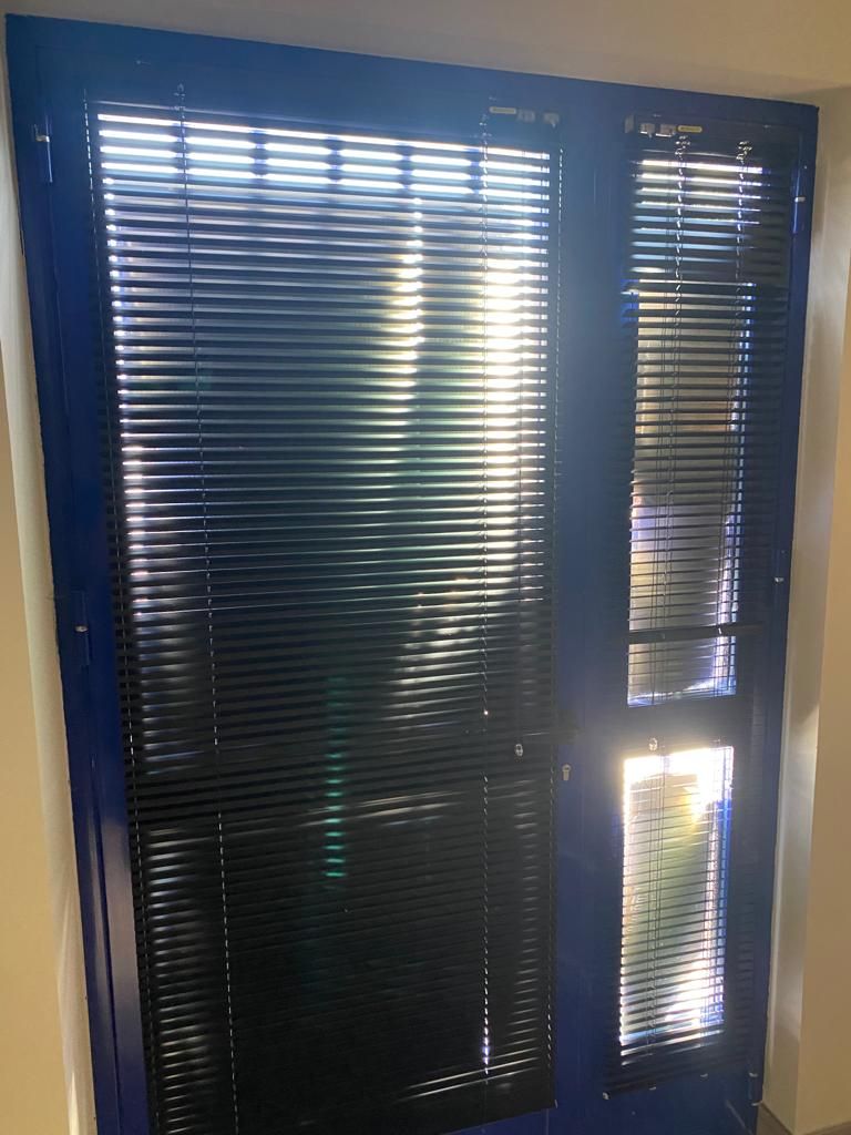 Persianas oscuras con luz solar que se filtra a través de estrechas lamas y una luminosa abertura vertical a la derecha.