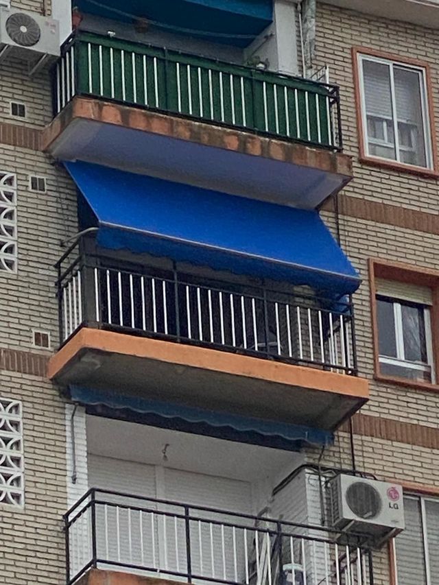 Balcones de apartamentos con toldos azules y barandillas verdes en un edificio de ladrillo.