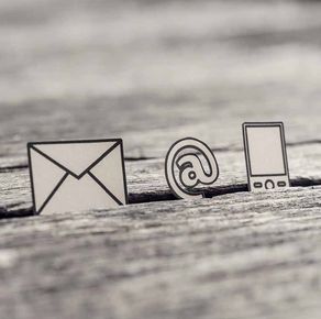 Sobre, símbolo @ e iconos de smartphone sobre una superficie de madera, que representan el correo electrónico y la comunicación móvil.