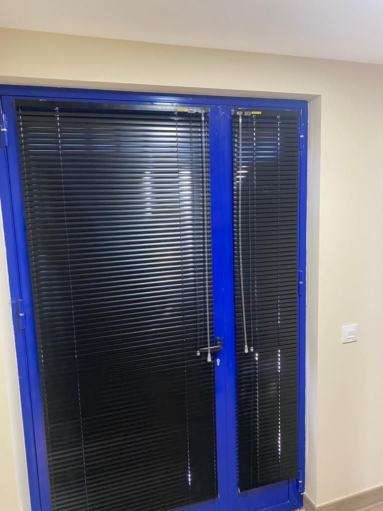 Puerta de cristal con marco azul y persianas negras cerradas en una habitación de color beige.
