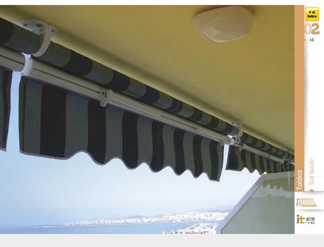 Un toldo a rayas negras y grises bajo un techo amarillo, con vistas a un luminoso paisaje costero.