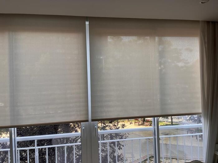 Persianas beige cerradas sobre una ventana de balcón con una barandilla blanca en el exterior.