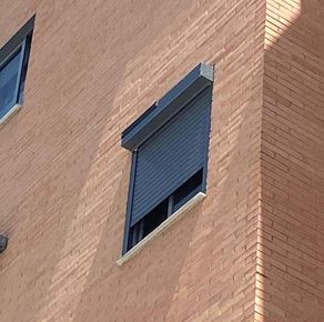 Esquina de un edificio de ladrillo con una persiana oscura parcialmente cerrada.