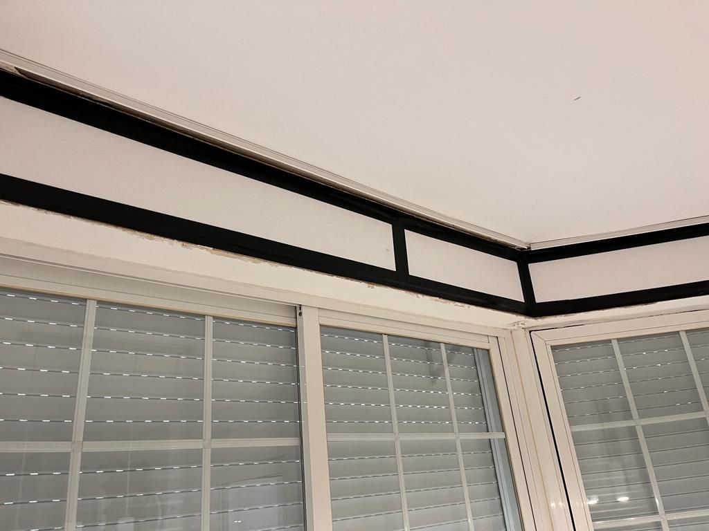 Rincón blanco de una habitación con persianas cerradas y molduras negras en el techo.