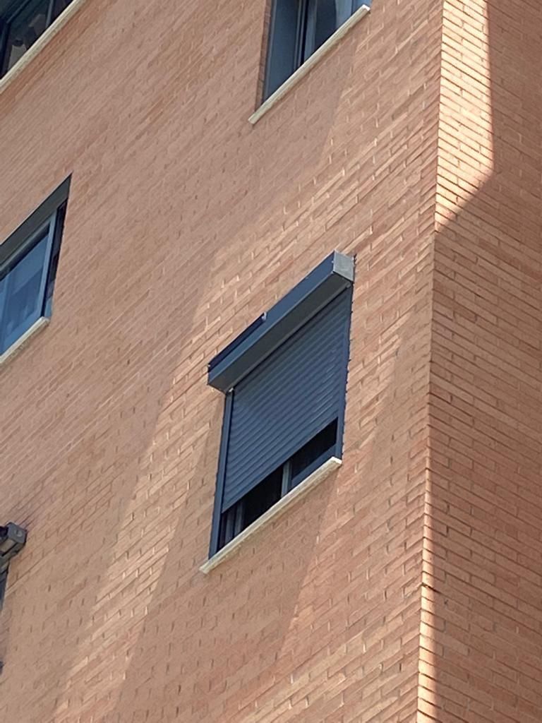 Edificio de apartamentos de ladrillo con ventanas azules y una persiana gris parcialmente bajada.