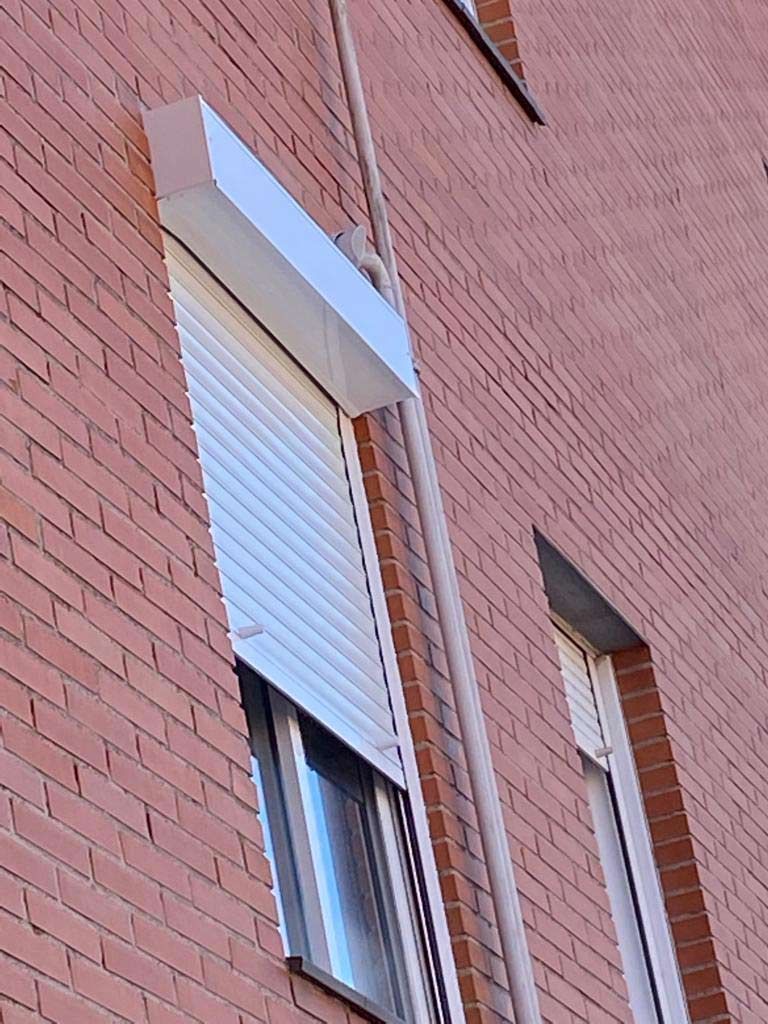 Fachada de ladrillo con una contraventana blanca y otra ventana abierta debajo.