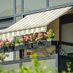 Toldo a rayas sobre una jardinera de balcón llena de flores rosas en la fachada de un edificio.