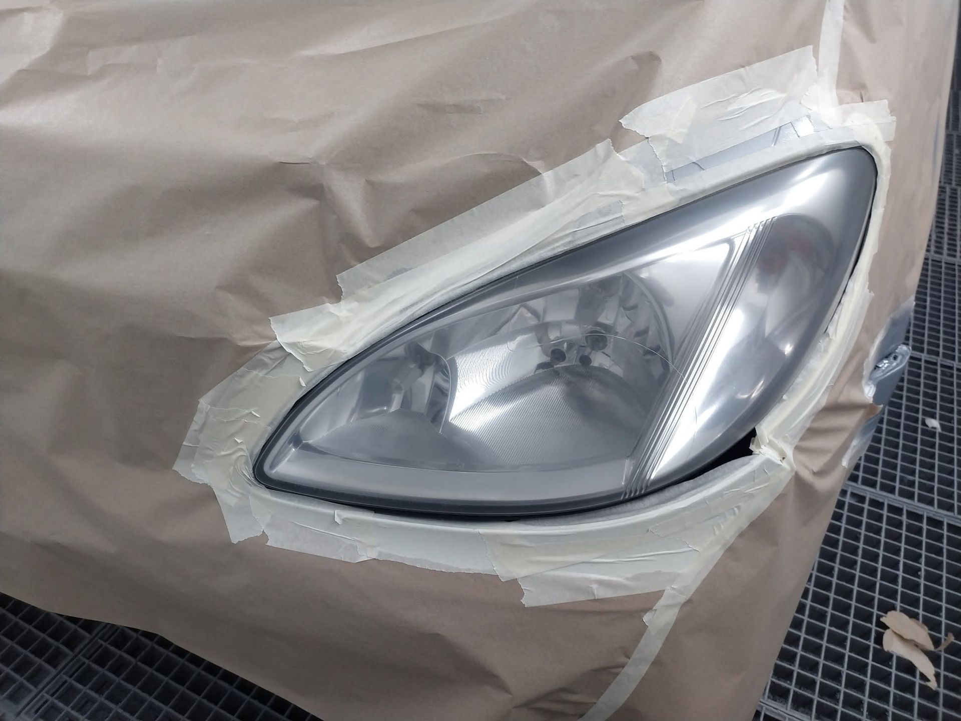 Du ruban de masquage recouvrant un phare de voiture à l’avant d’un véhicule protégé avec du papier kraft.