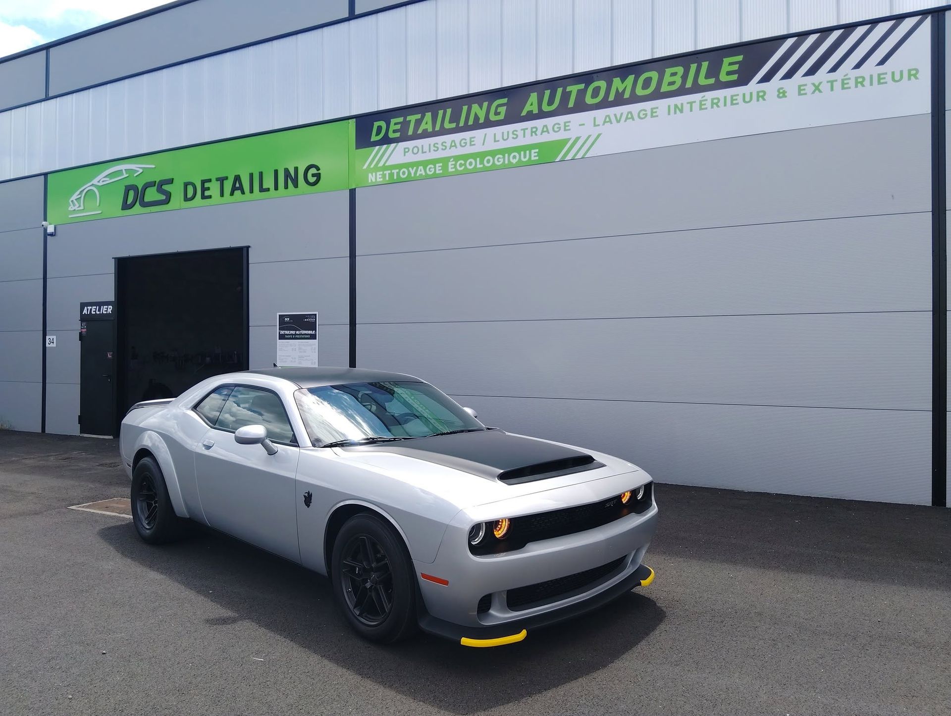 Voiture de sport argentée garée devant un atelier de detailing doté d’une grande porte de garage.