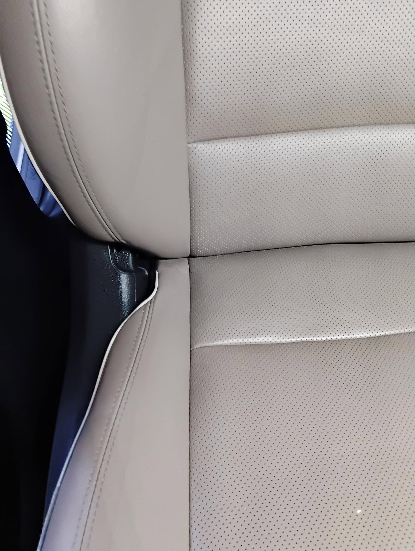 Siège de voiture avec des surpiqûres apparentes et un revêtement perforé, montrant une couture près du panneau latéral.