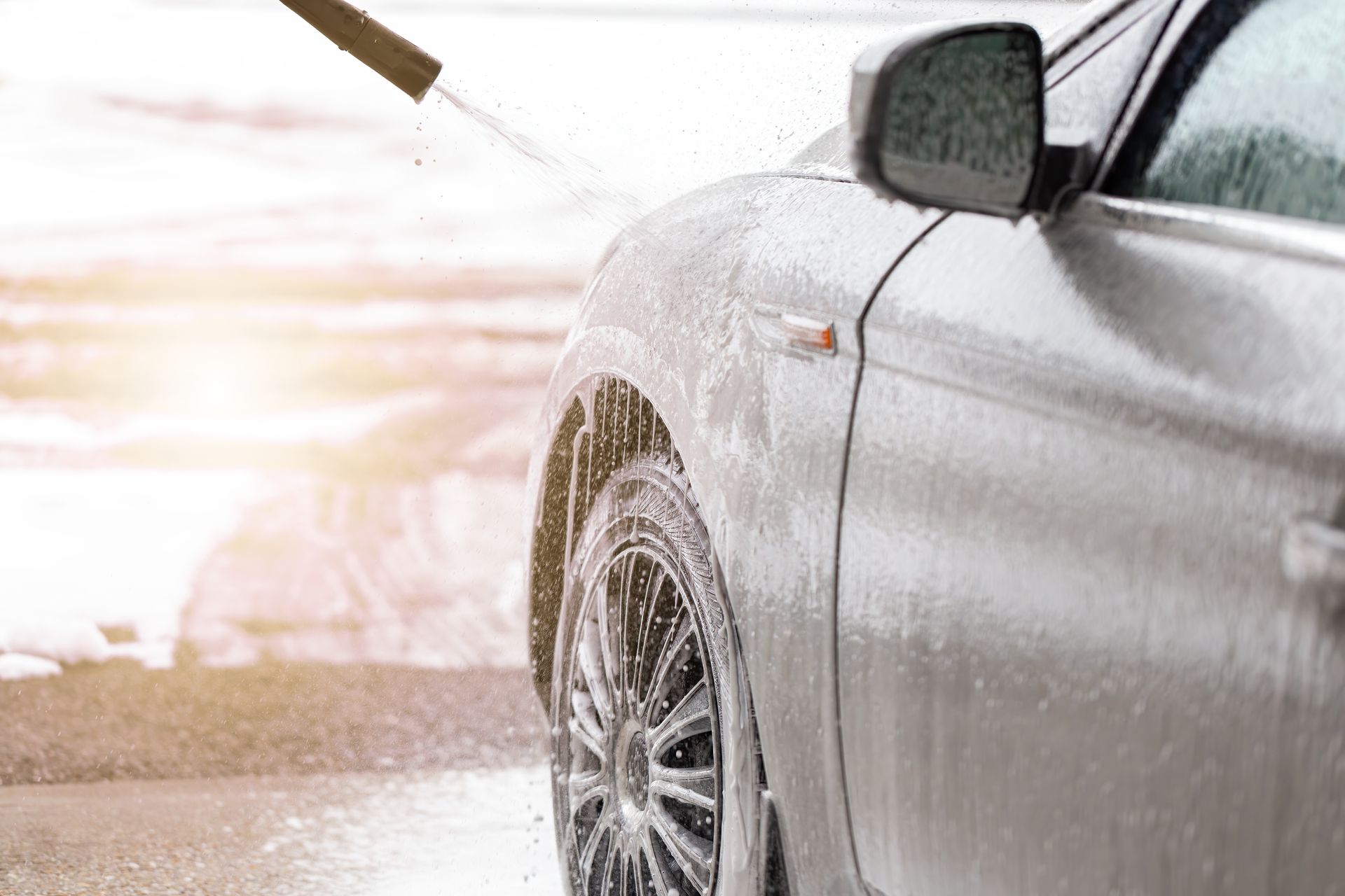 Voiture argentée arrosée pendant un lavage, avec de la mousse et un tuyau.