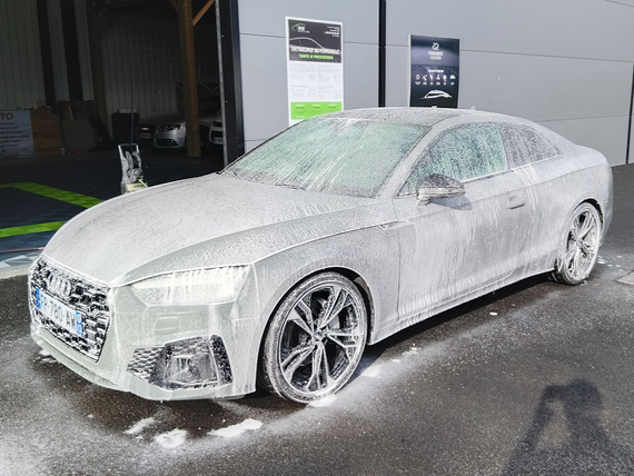 Berline recouverte de mousse dans une station de lavage.