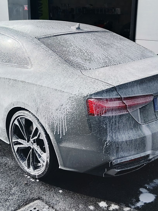 Coupé argenté recouvert de mousse dans une station de lavage.