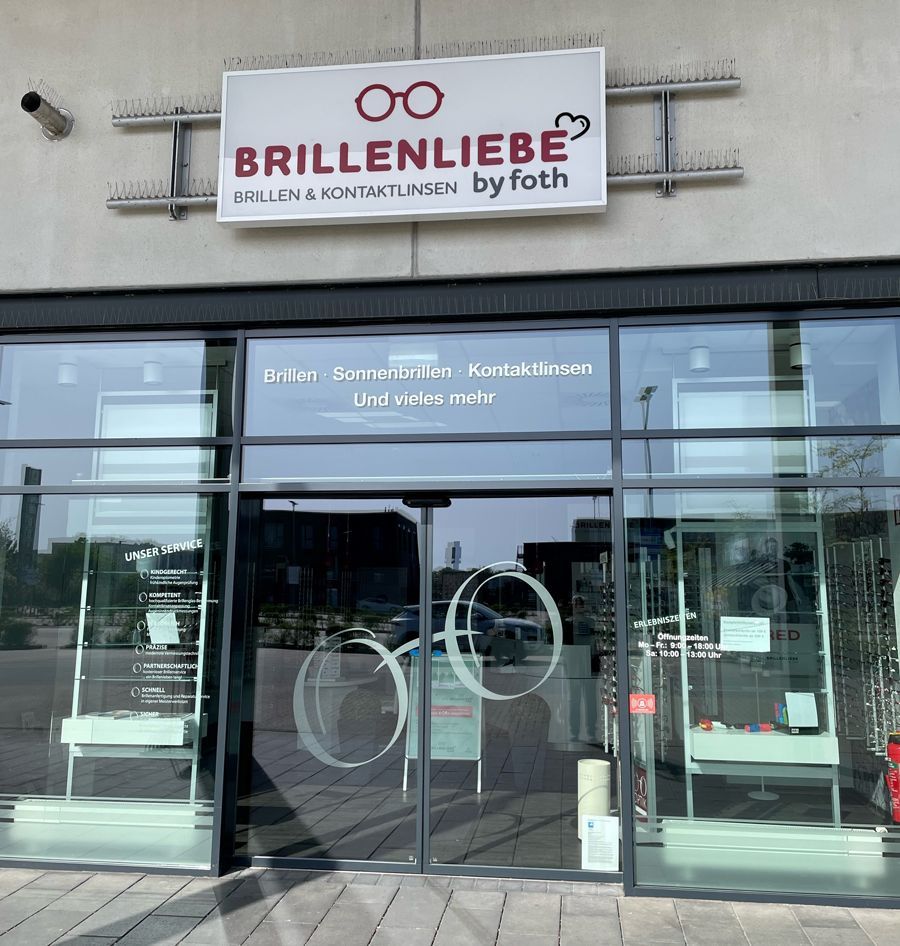 Schaufenster des Optikergeschäfts Brillenliebe mit Glastüren und rot-weißem Schild