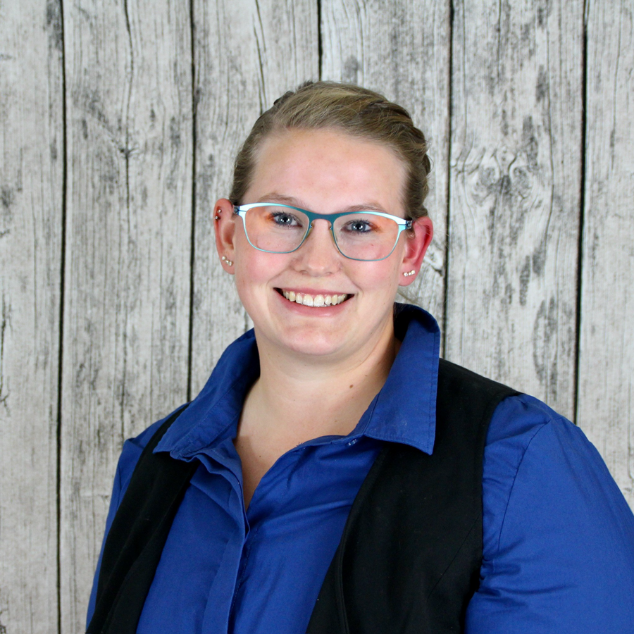 Lächelnde Person mit Brille und blauem Hemd vor grauem Holzhintergrund