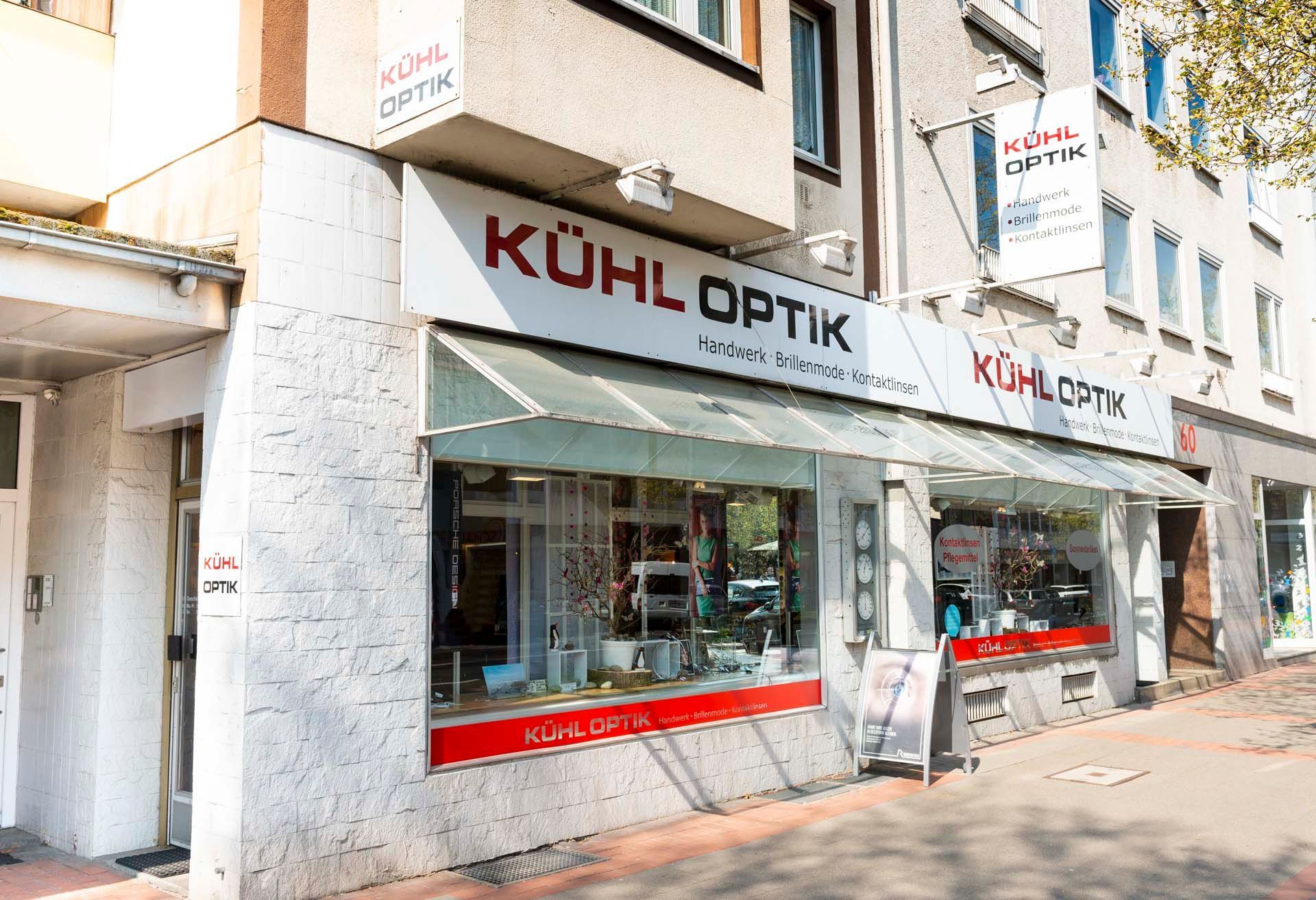 Das Kühl Optik-Geschäft mit großen Fenstern, weißer Fassade und roter Beschilderung an einer sonnigen Straße